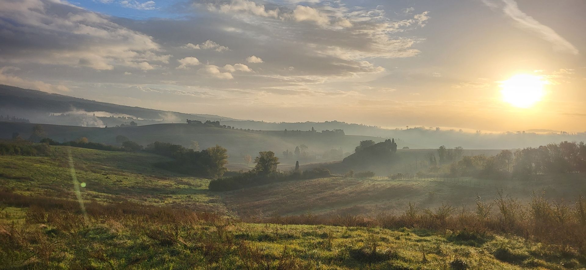 Panorama mattutino dalla strada per Vinci, al mattino. Con il sole che sorge dalla collina, il foliage autunnale, un velo di foschia nel fondovalle.