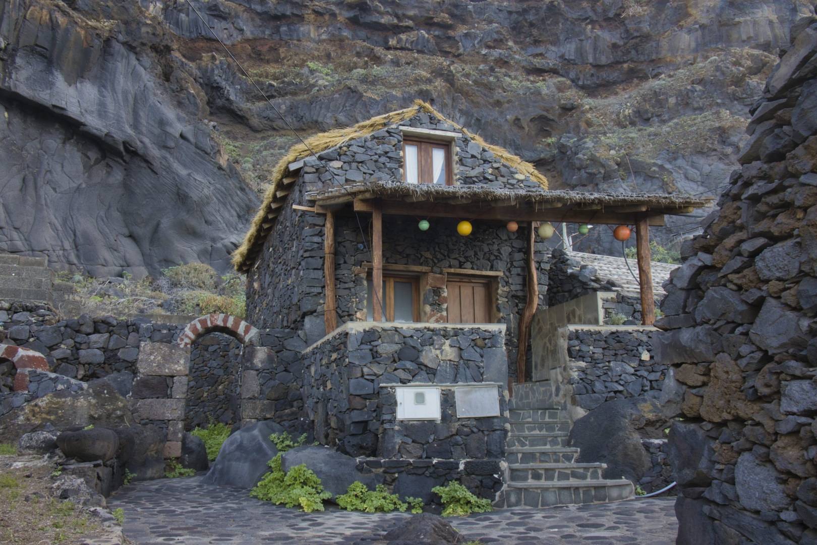 Casa di pietra vulcanica con tetto di paglia, a ridosso di una scogliera di roccia vulcanica