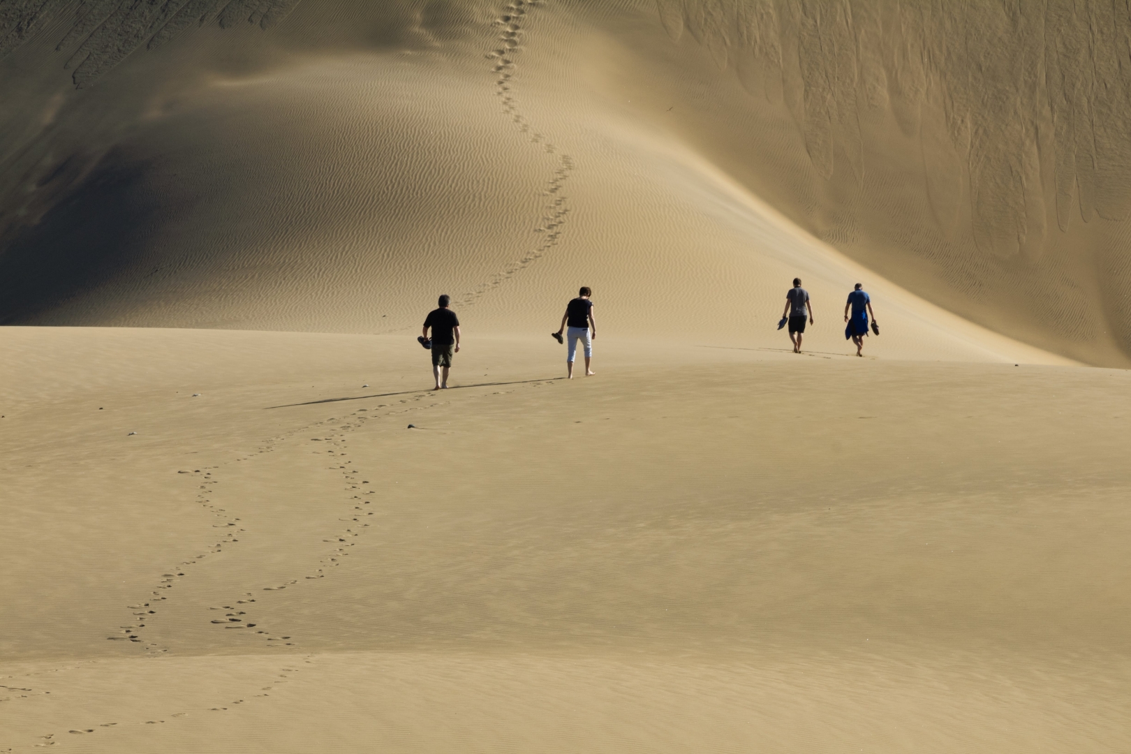 Quattro figure umane, in lontananza, si incamminano sulla sabbia verso una duna enorme che occupa tutta l'immagine.