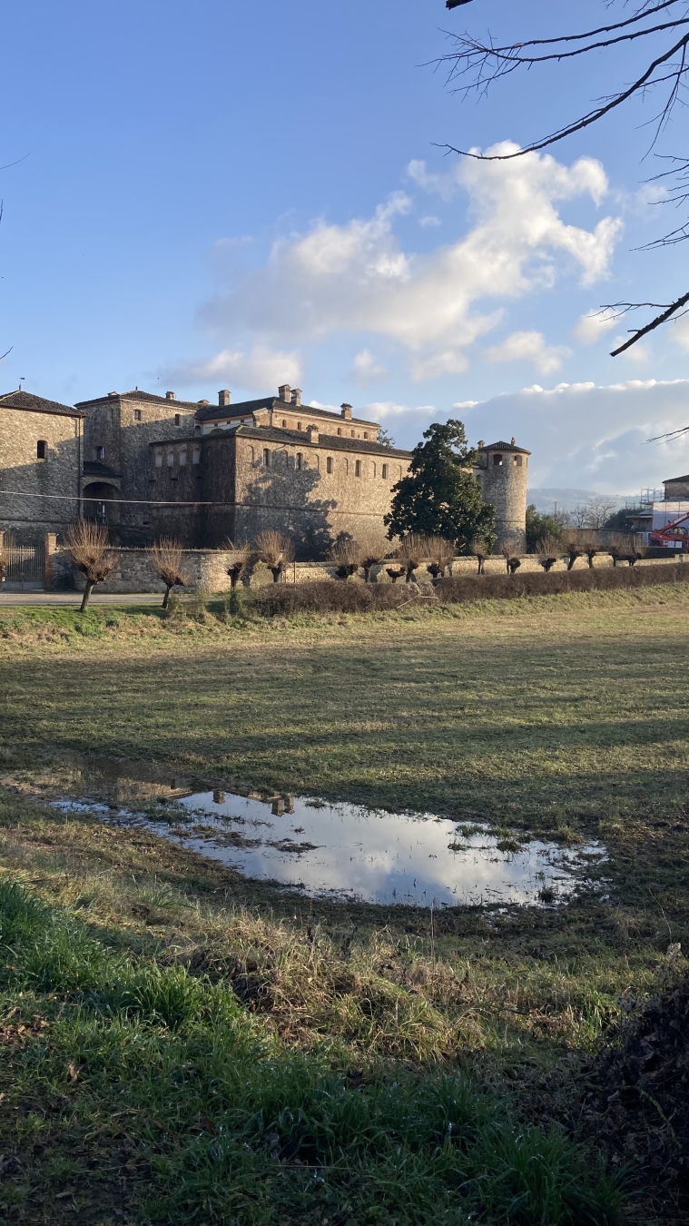 Agazzano Castle with spare clouds reflected in the water on the ground