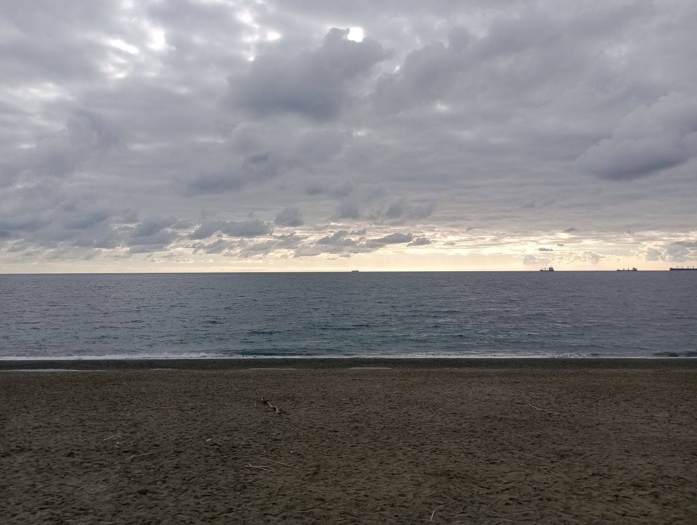 Fotografia di spiaggia, mare e cielo nuvoloso con un barlume di luce all'orizzonte