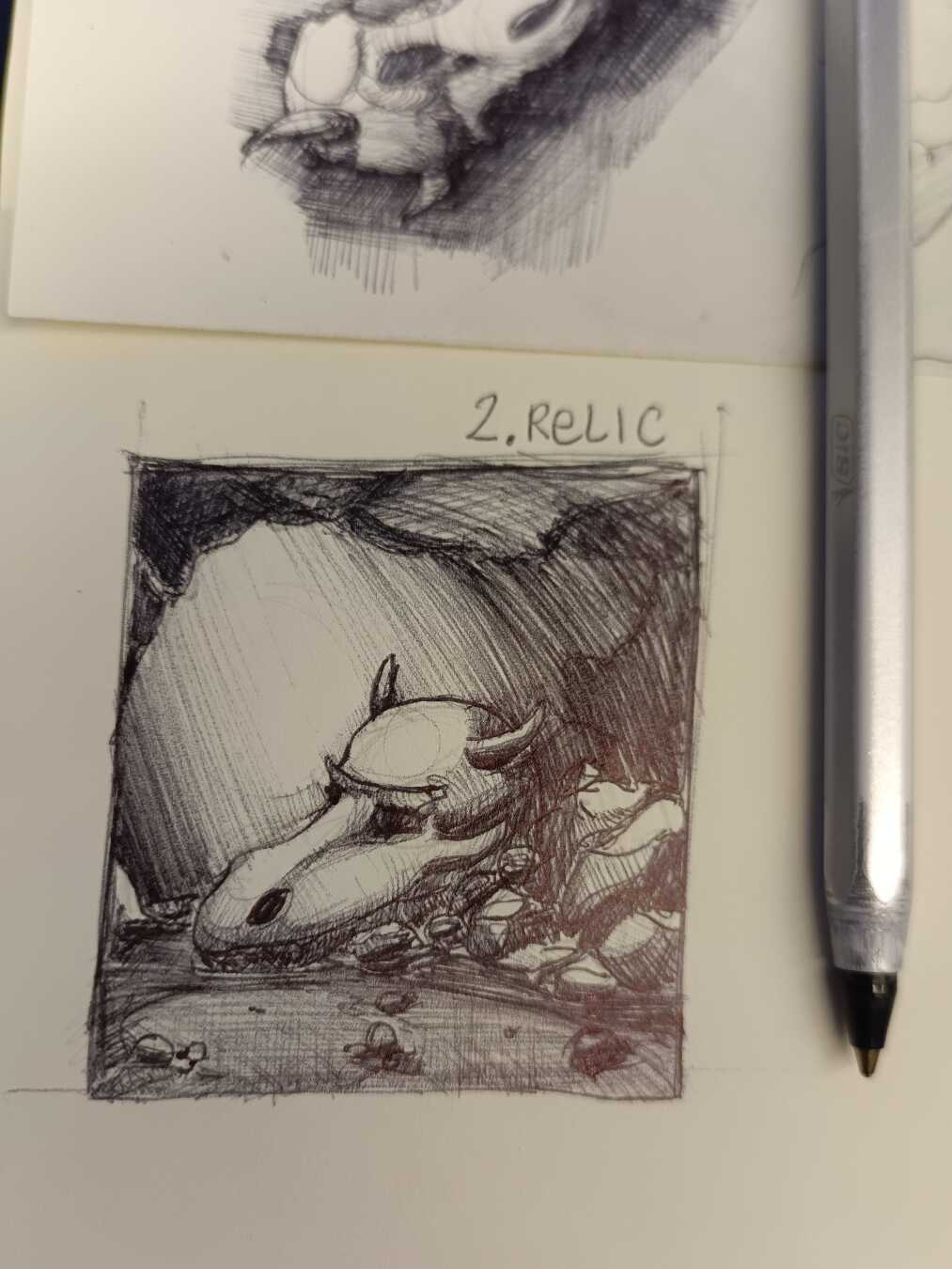 Disegno a penna di un teschio di drago come se fosse un ritrovamento in un ambiente tipo grotta tra delle rocce. Si vede anche la penna bic sul lato destro e una parte di un altro schizzo sullo sfondo.